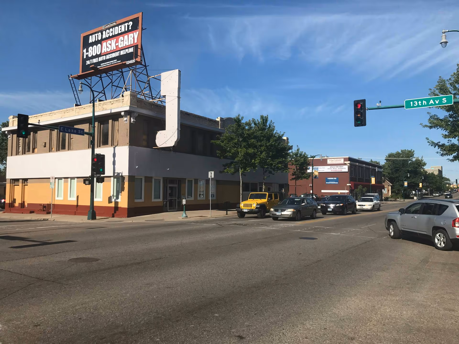 Corner street scene showing a two-story building, a large billboard, and parked cars.