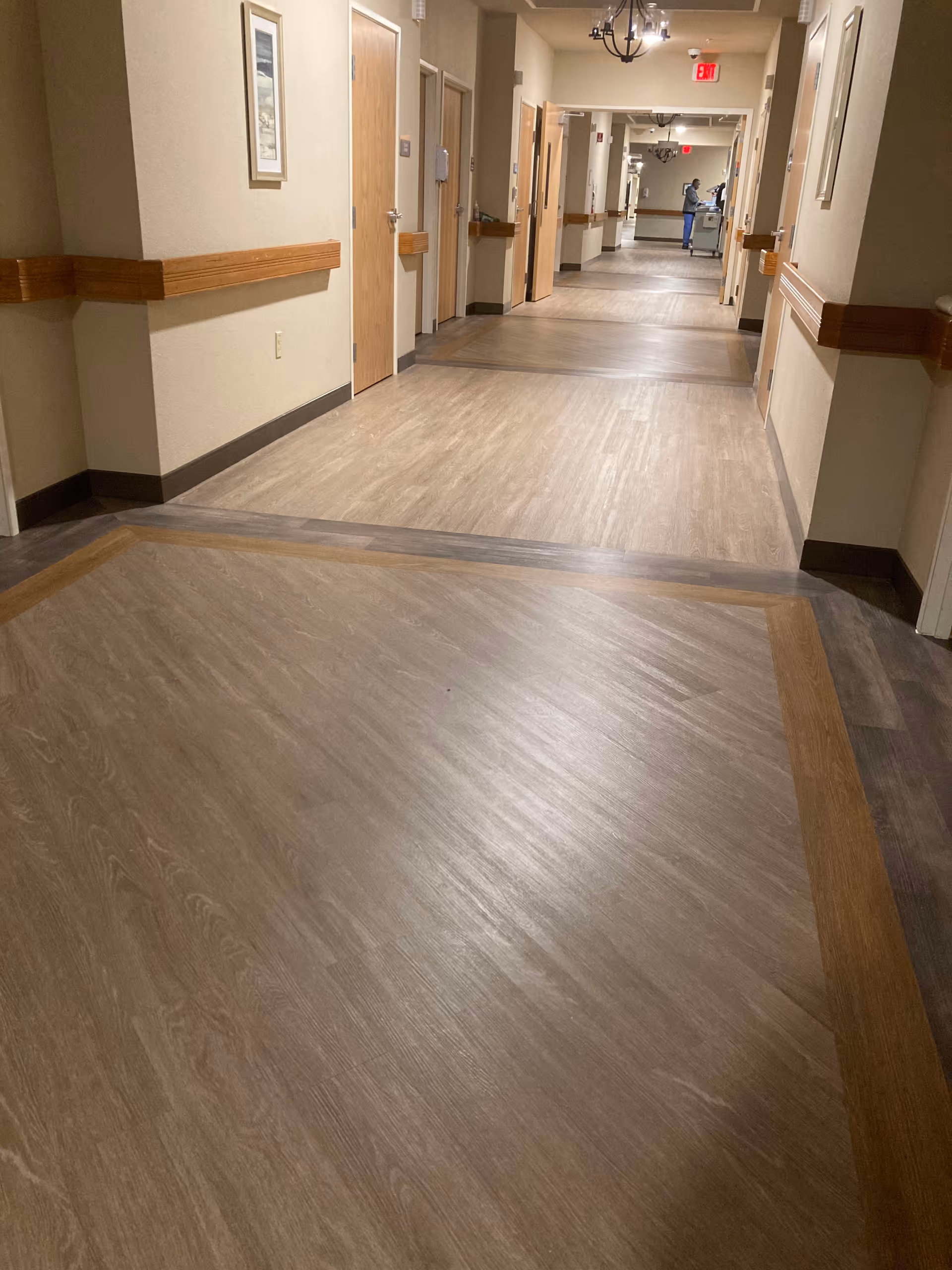 Long, well-lit corridor of a senior living facility with doors and wall-mounted handrails.