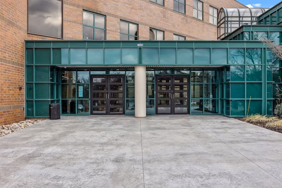 Front entrance with double glass doors, green-framed facade, brick exterior.