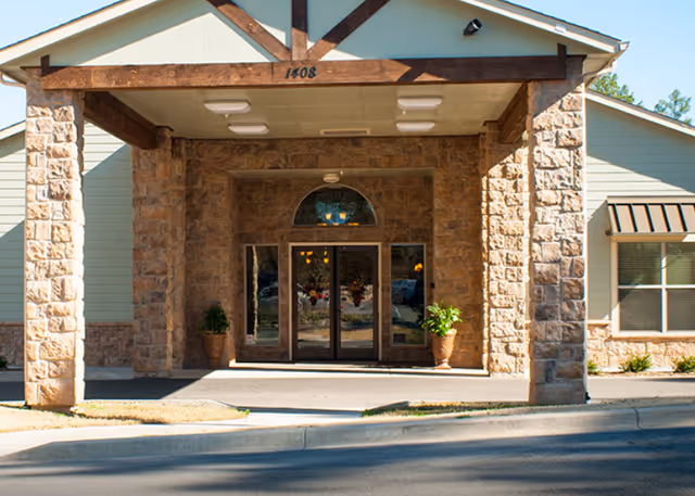 Stone entrance with a covered portico, glass doors, and potted plants.