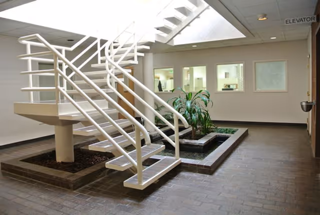 Interior lobby featuring a white staircase over a planter, with elevator sign in background.