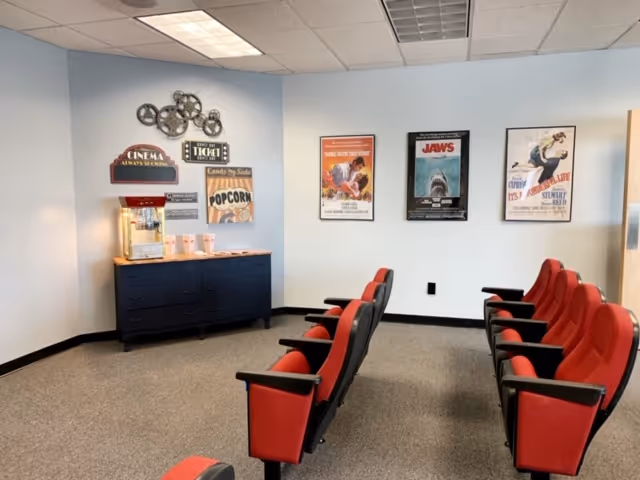 A small cinema room with red seats, movie posters, and a popcorn station.