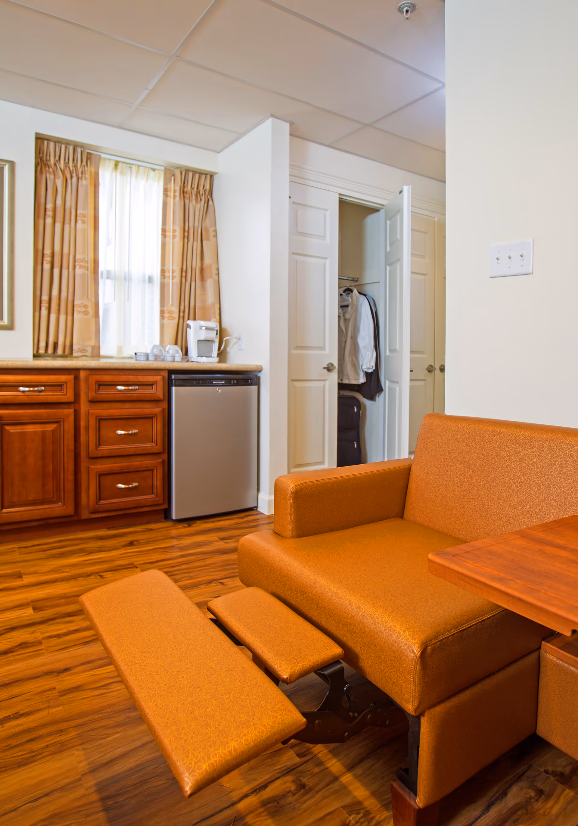 Orange sofa and kitchenette with a fridge, closet with clothes, and wood floors.