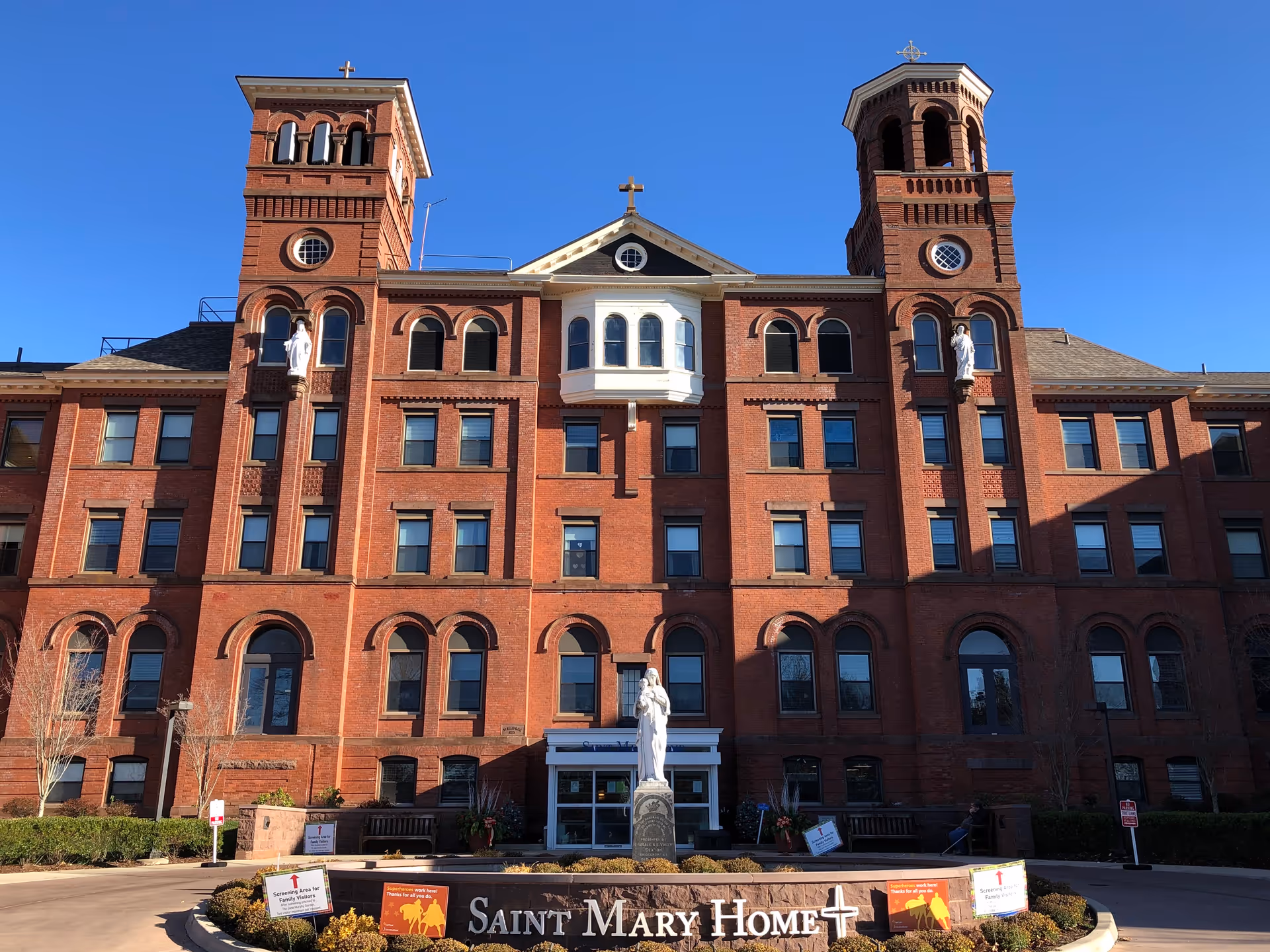Front view of red brick senior living facility with twin towers and statue.