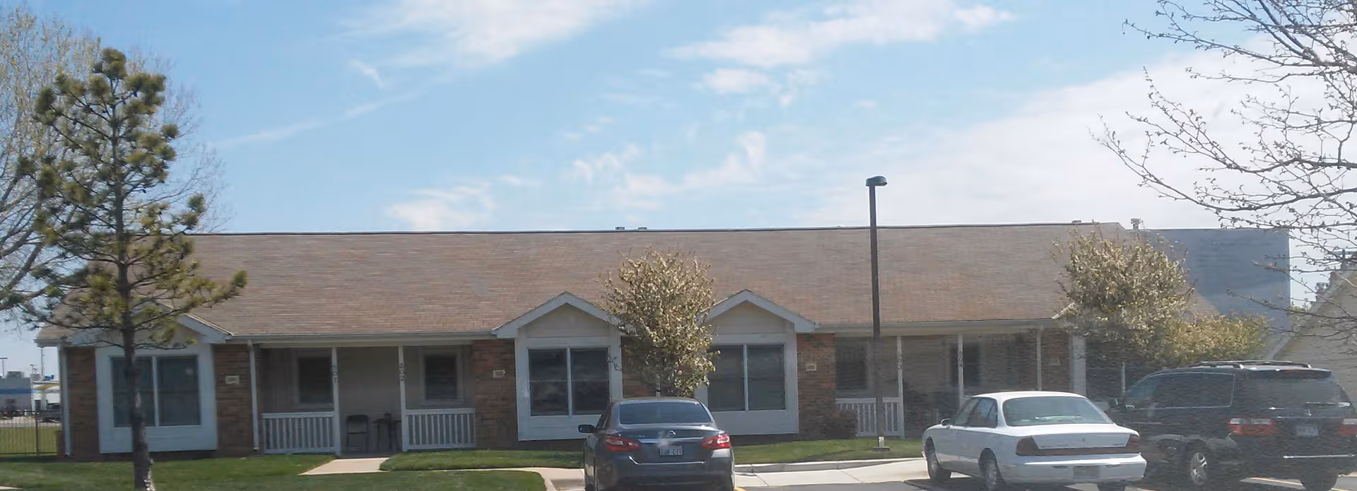 Exterior of a single-story brick senior living residence with cars in the parking lot