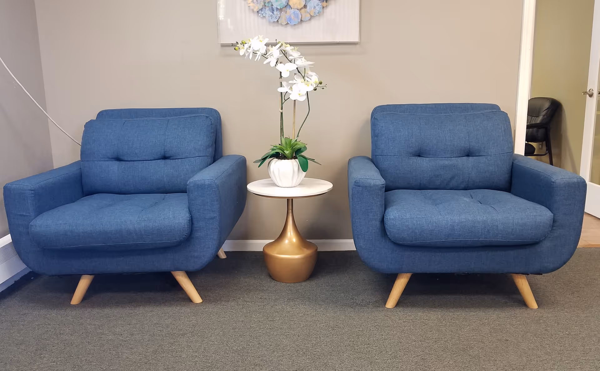 Two blue armchairs flank a small round table with a potted orchid