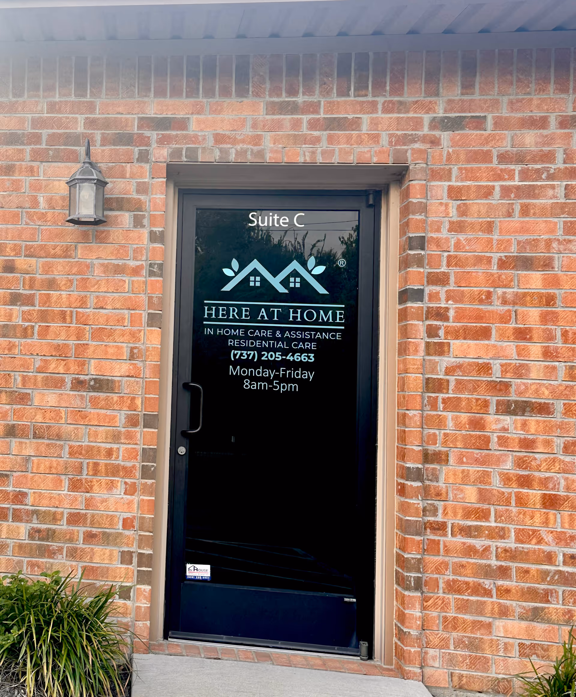 Brick exterior wall with a black door labeled Suite C and Here At Home logo.