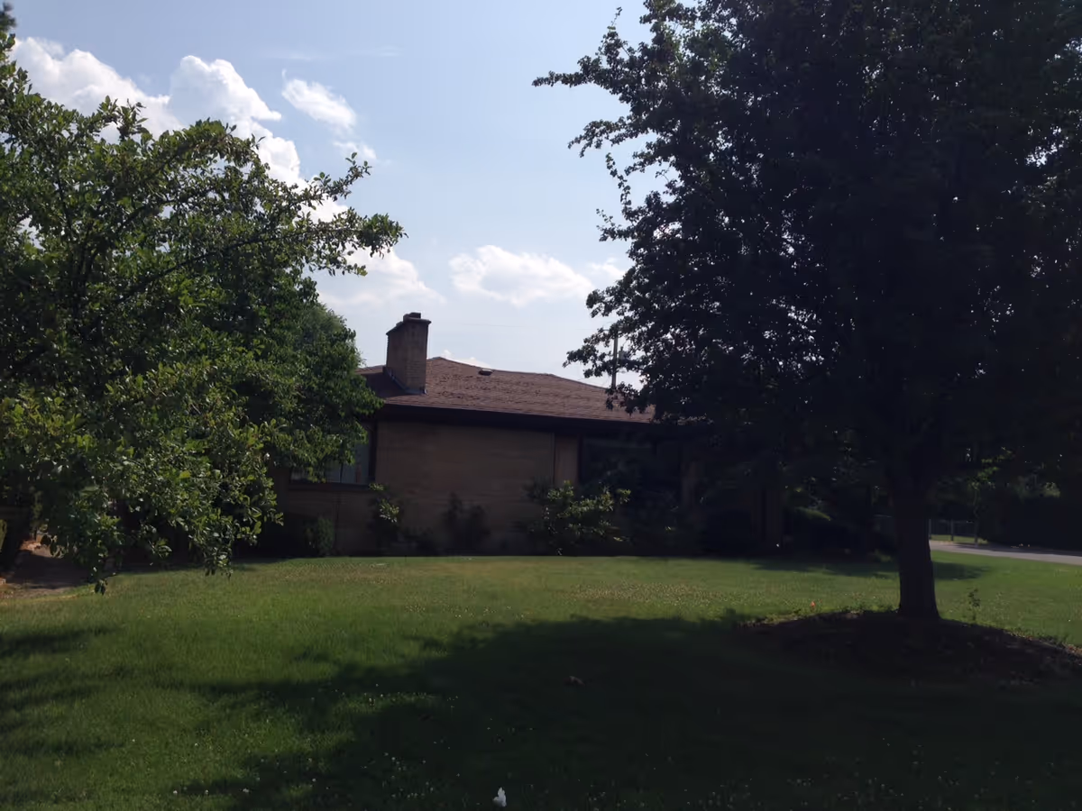 Exterior view of a single-story home-like facility with green lawn and trees.