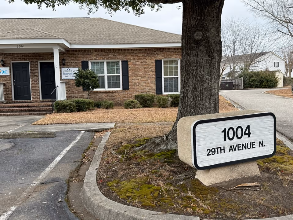 Exterior brick building of Home Care Helpers USA with address sign and parking.