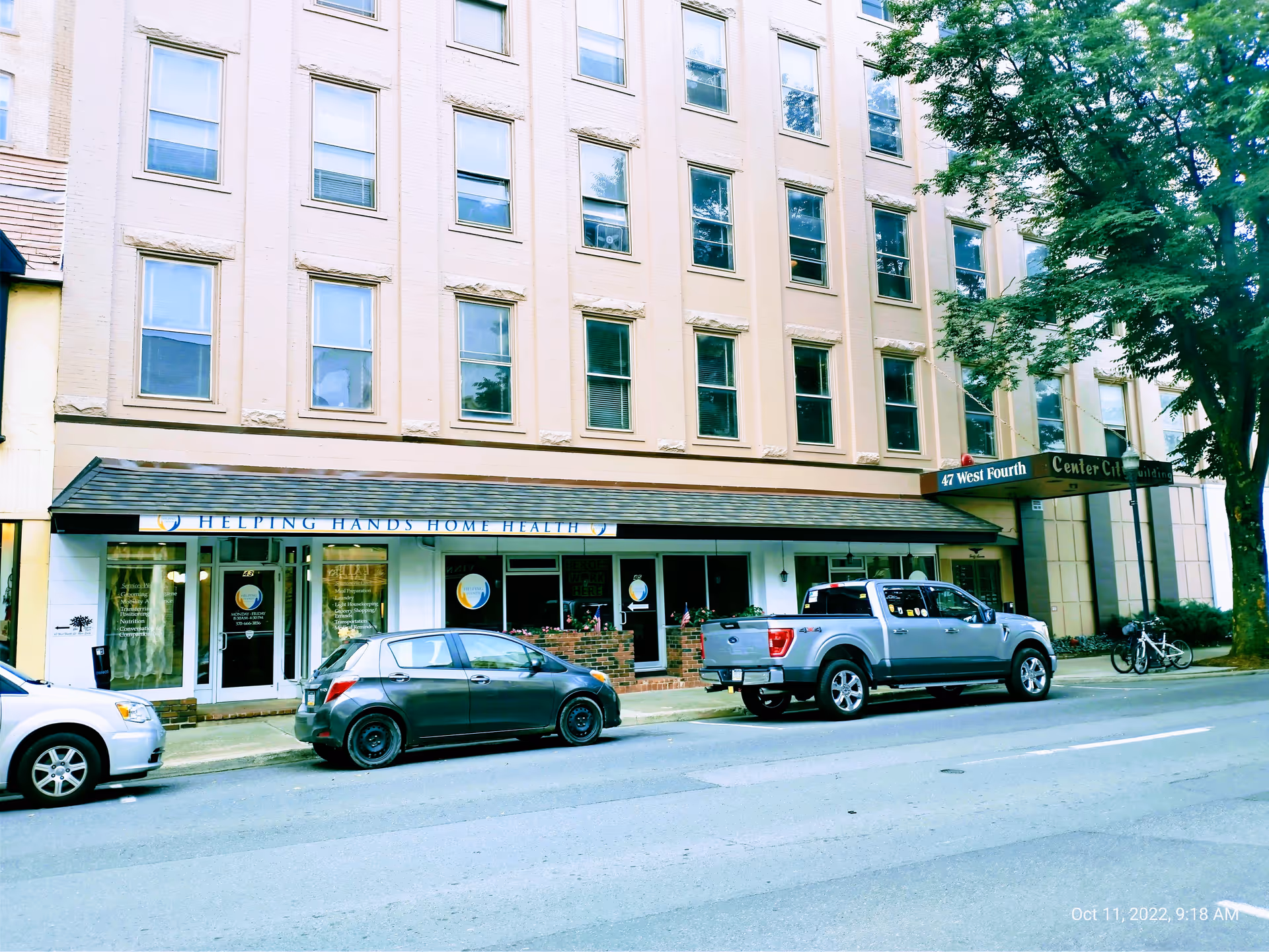 Beige multi-story building with Helping Hands Home Health storefront on a street.