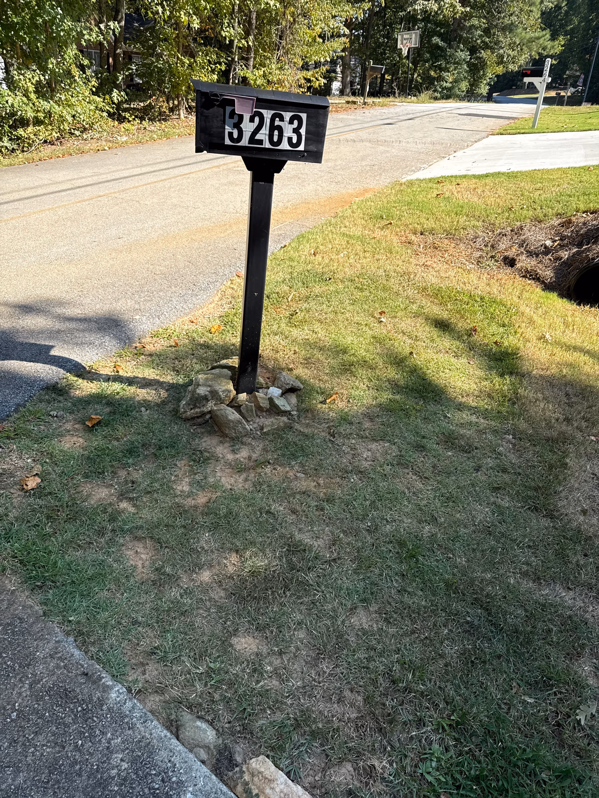 Black mailbox with large white numbers on a grassy curb beside a street.