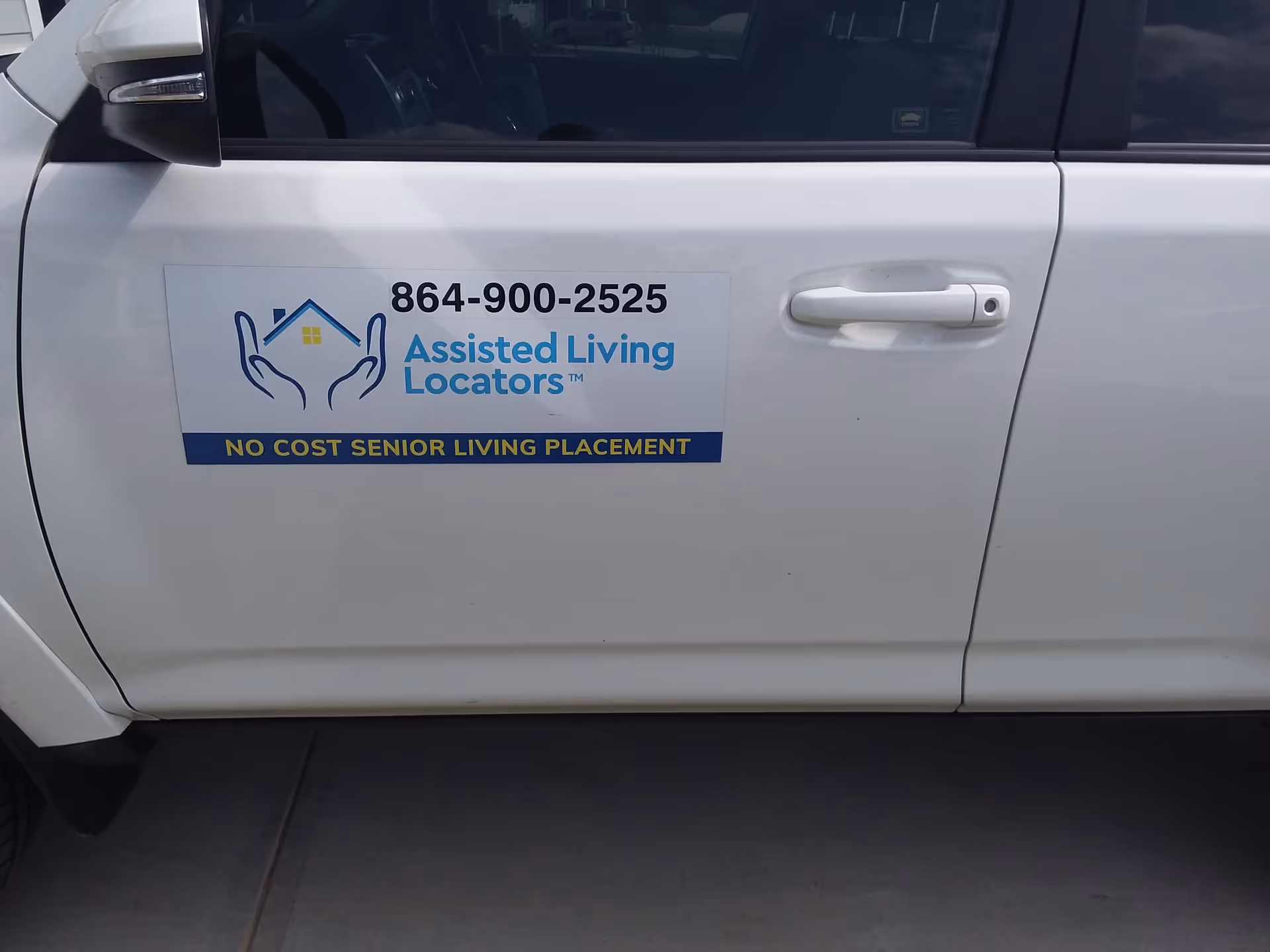 White vehicle door displays Assisted Living Locators sign with phone number.
