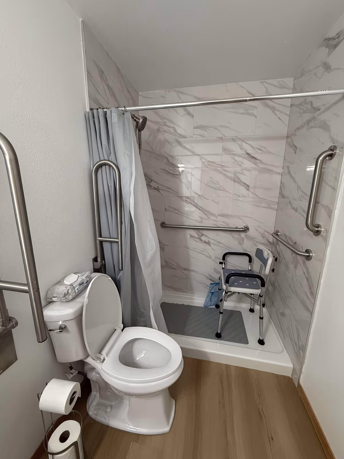 Accessible bathroom with toilet, shower stall, grab bars, and a folding shower chair.