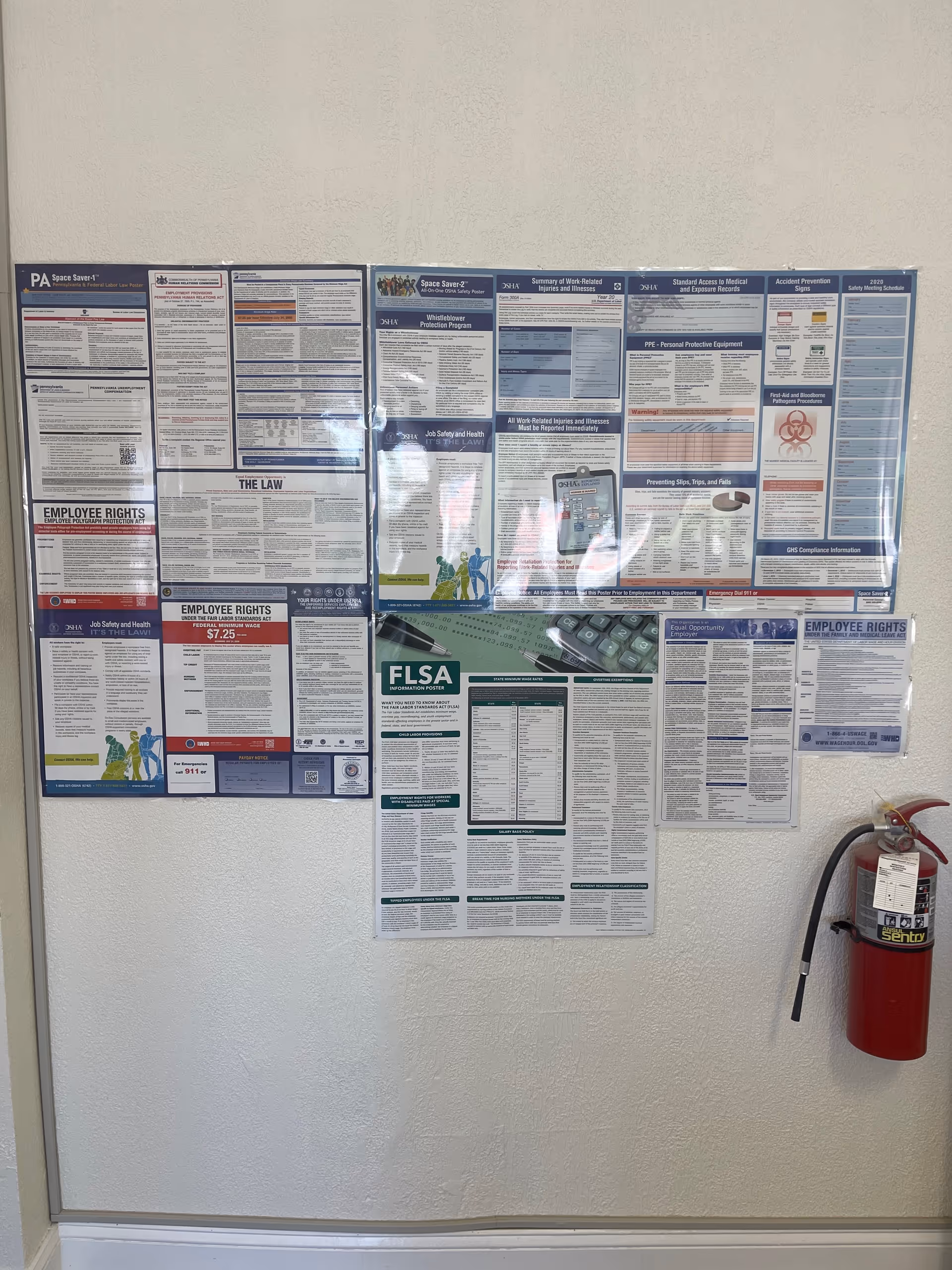 Bulletin board wall with multiple posted notices and a red fire extinguisher nearby.