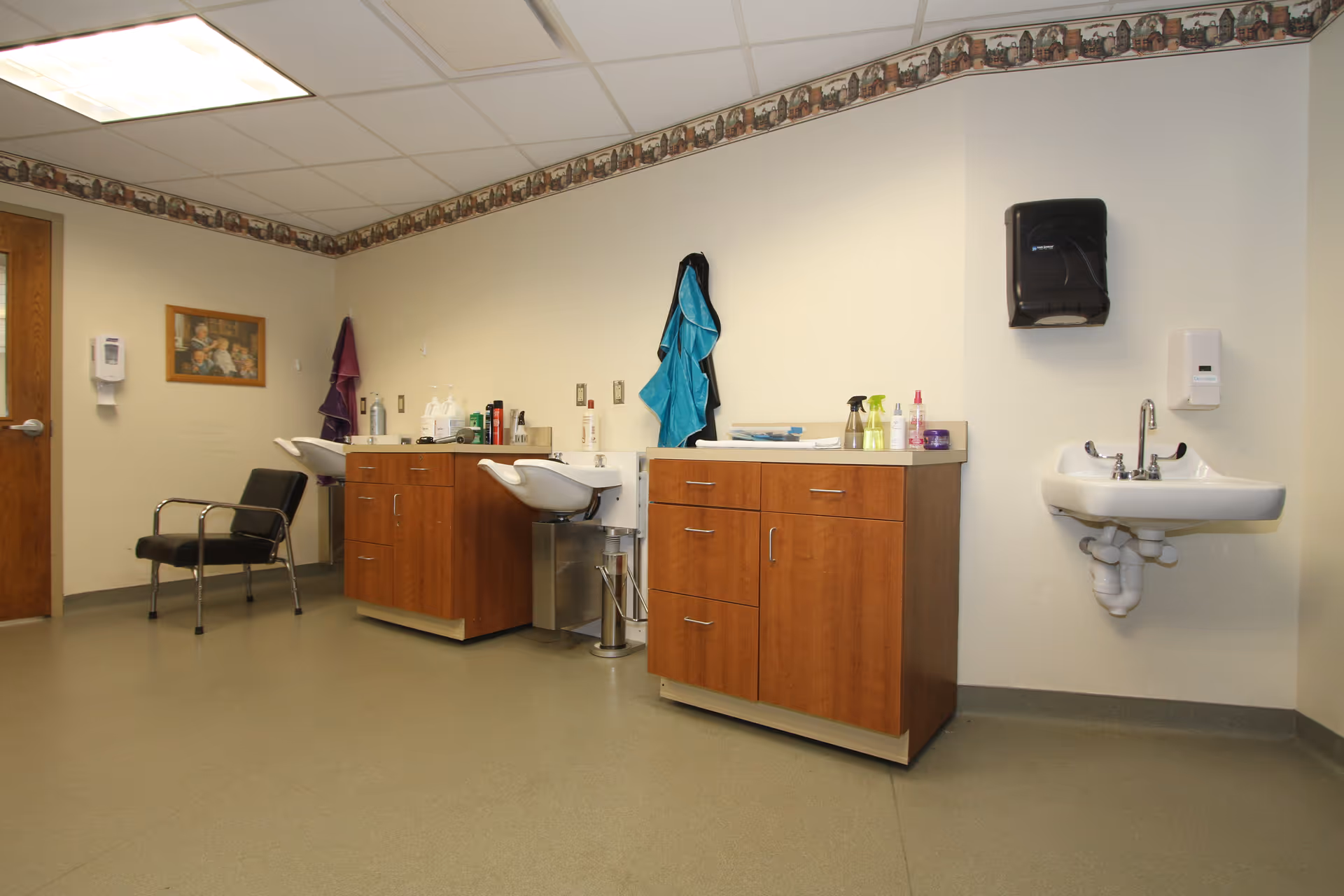 Interior of a senior living facility salon with sinks, cabinets, and chairs along the wall.