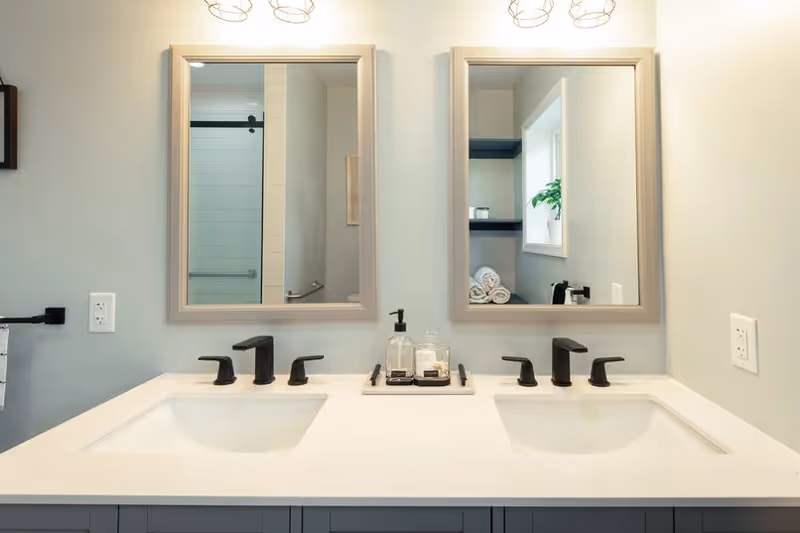 A double-sink bathroom vanity with two mirrors and soap dispensers.
