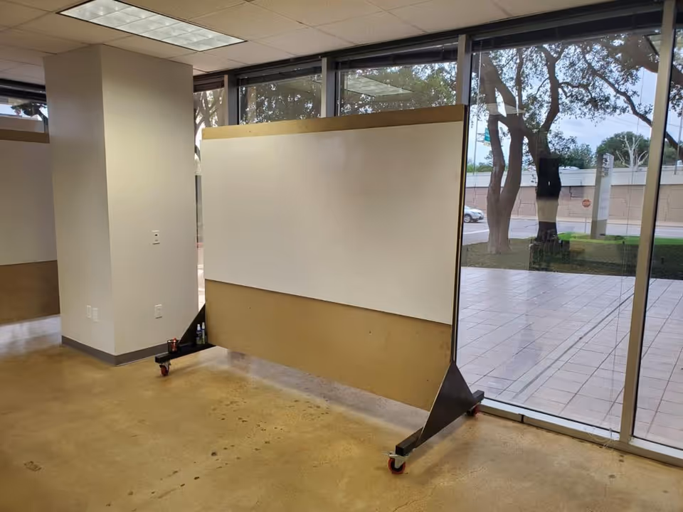 Interior space with a portable whiteboard on wheels near floor to ceiling glass windows.