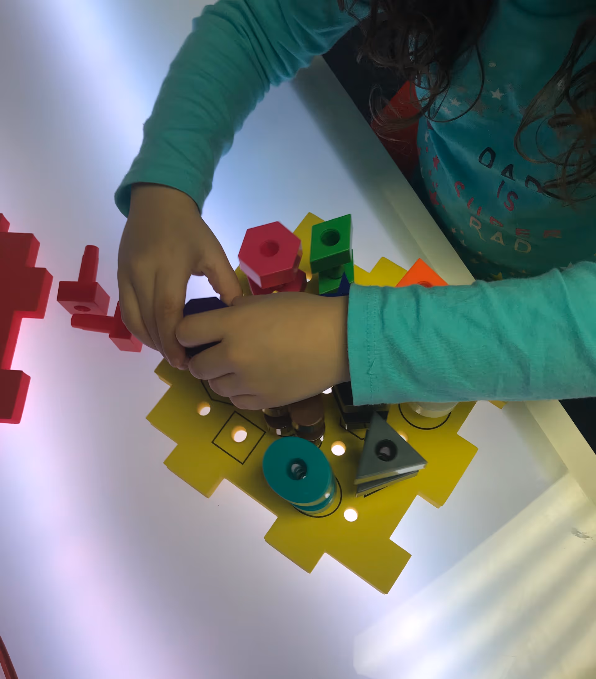 Close-up of a child's hands assembling colorful geometric blocks on a yellow tray.
