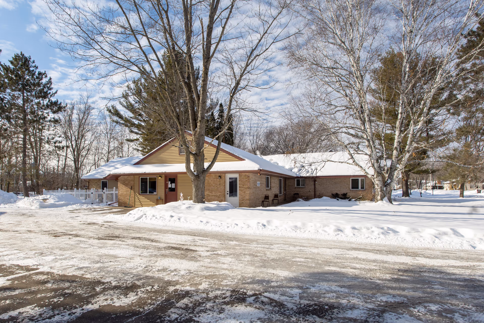 Snow-covered, single-story brick building with bare trees and a clear driveway.
