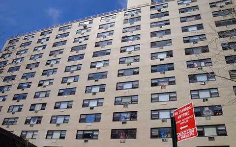 Tall beige senior housing building exterior with numerous windows and a no standing sign.