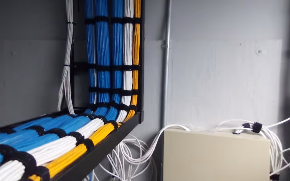 Color-coded cables run along a rack and a beige electrical box in a utility room.