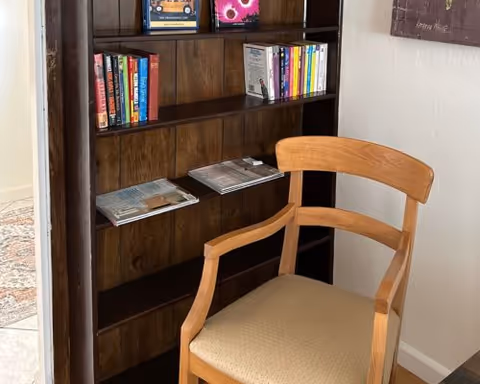 A wooden chair next to a bookshelf stocked with magazines in a hallway.