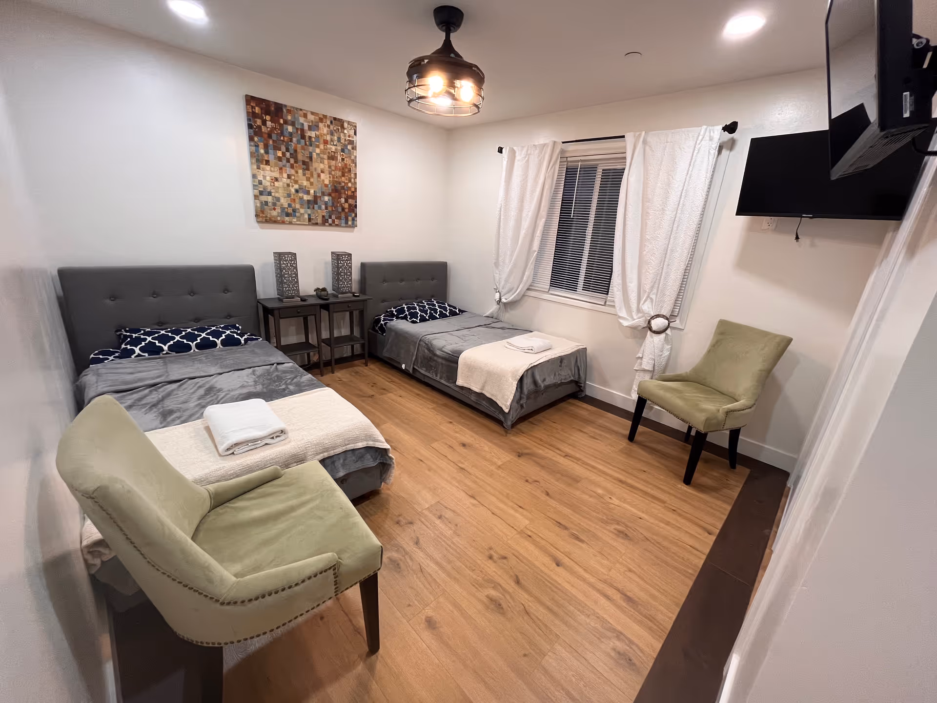 Two twin beds with tufted headboards, chairs, and a window in Pioneer Care Home bedroom.