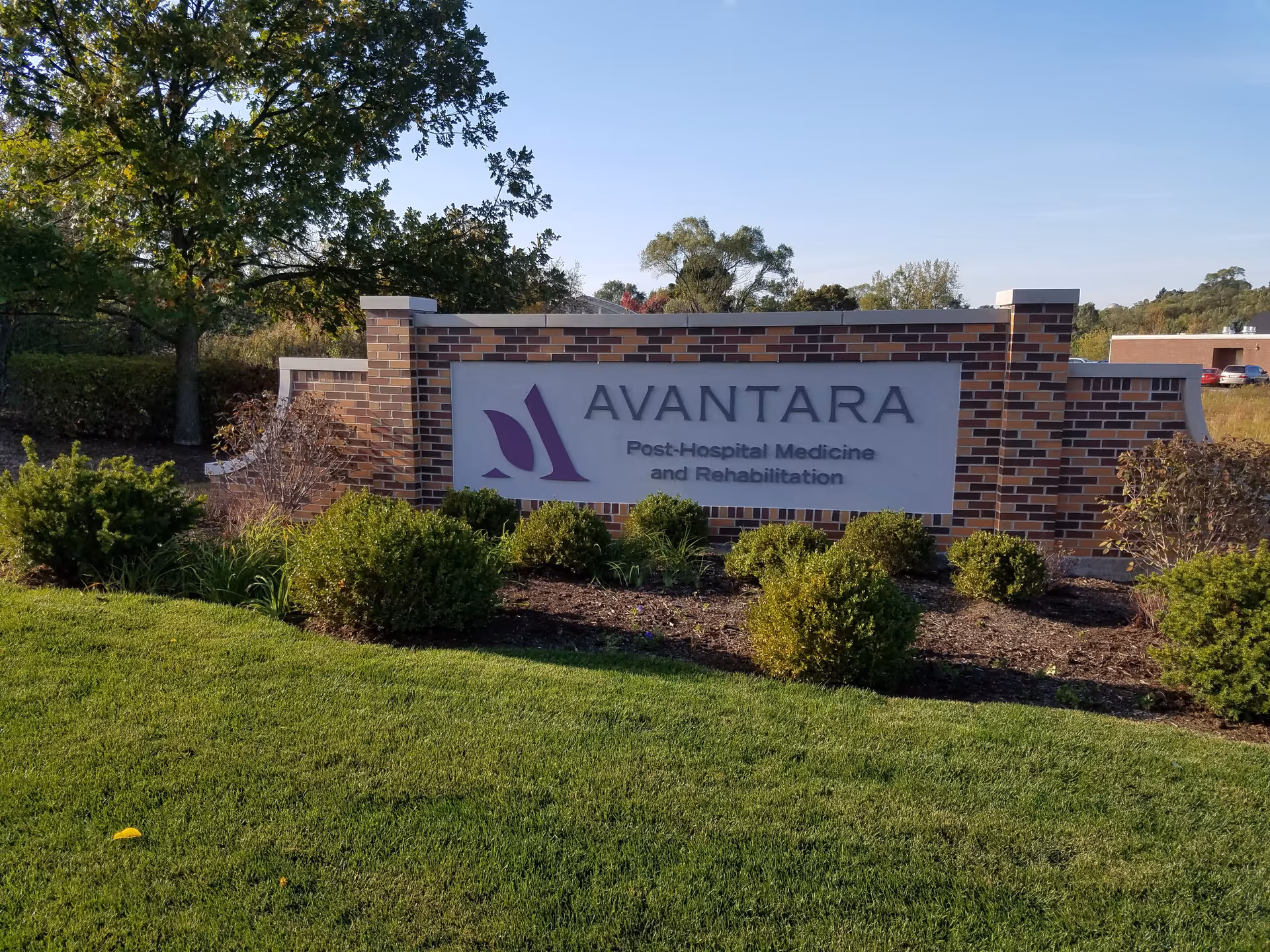 Outdoor brick sign reading AVANTARA with surrounding shrubs and trees nearby.