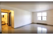 Empty rectangular room with a window, doorway to a bathroom, and tiled floor.