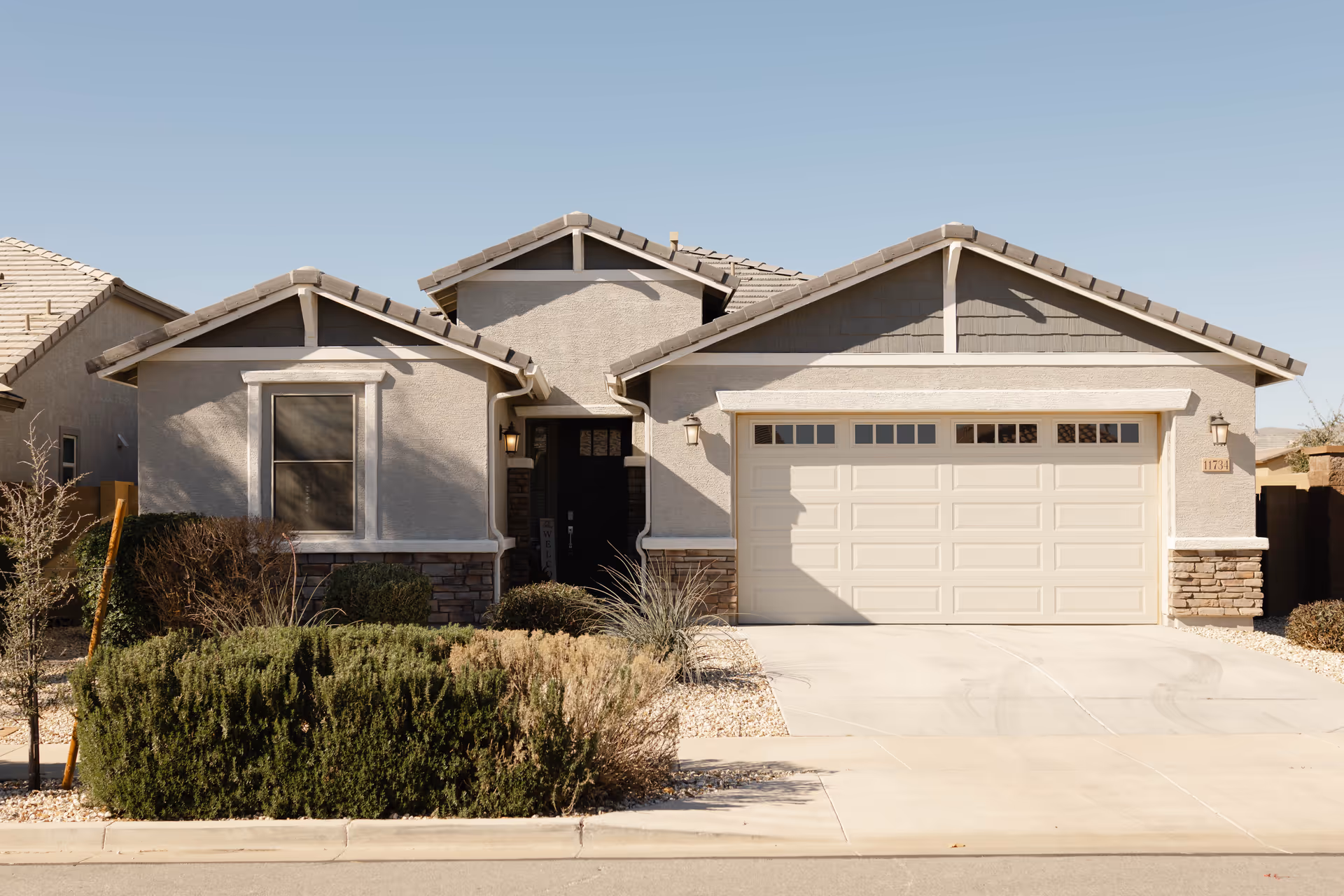 Front exterior of a beige, ranch-style house with a two-car garage and desert landscaping.