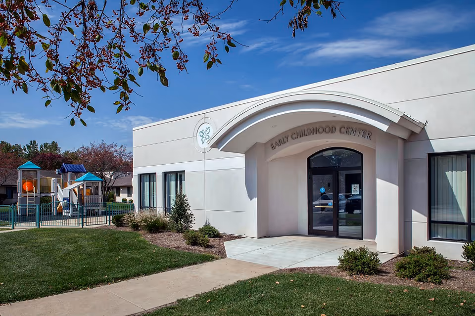 Exterior view of a light-colored building entrance with a playground to the left