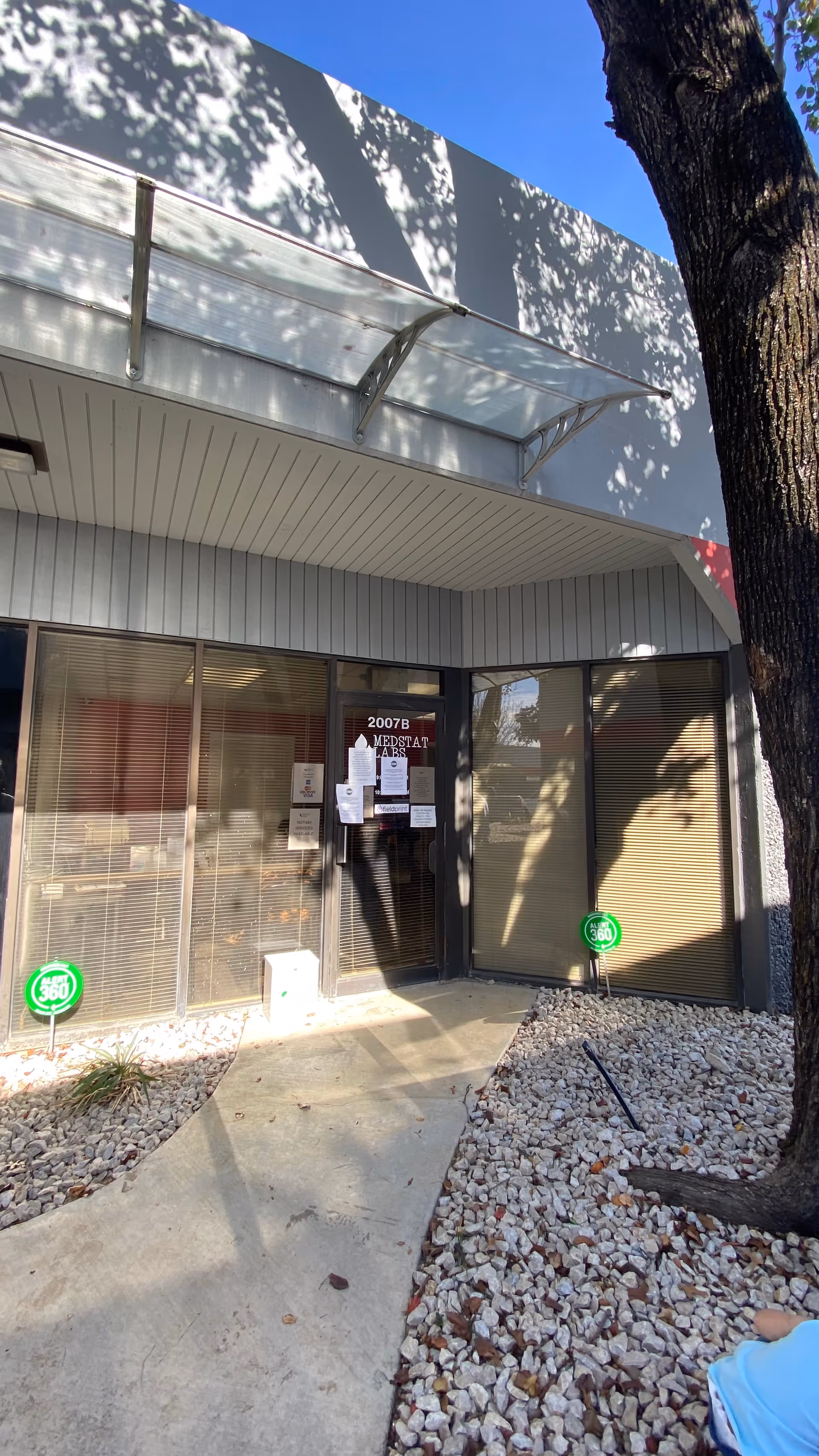 Exterior view of Medstat Labs entrance with glass doors and a tree nearby.