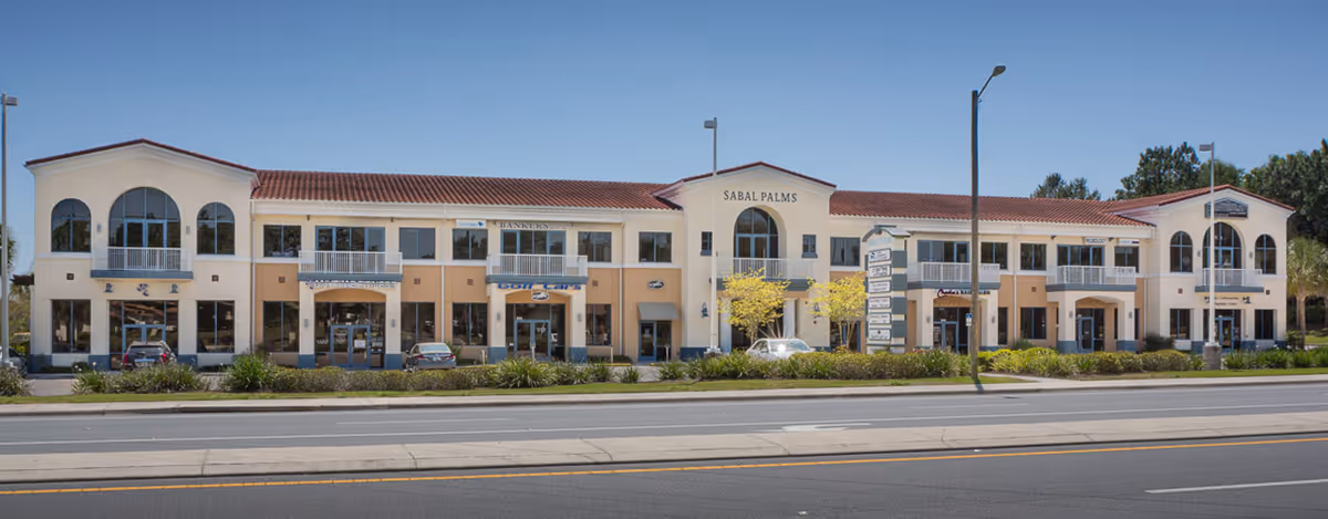 Two-story beige senior living facility facade along a street with parked cars.
