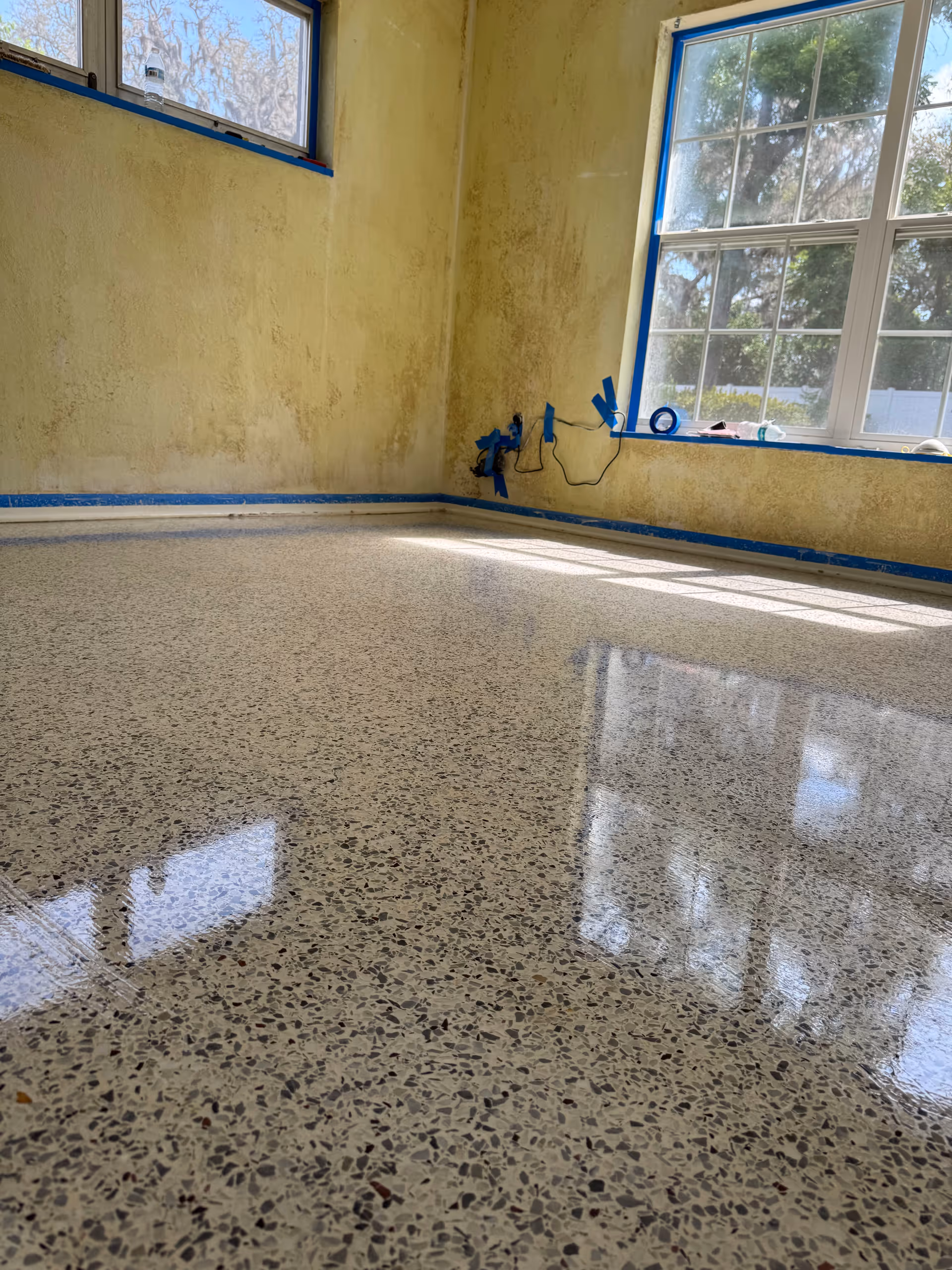 A partially renovated interior room with taped windows and a glossy terrazzo floor.
