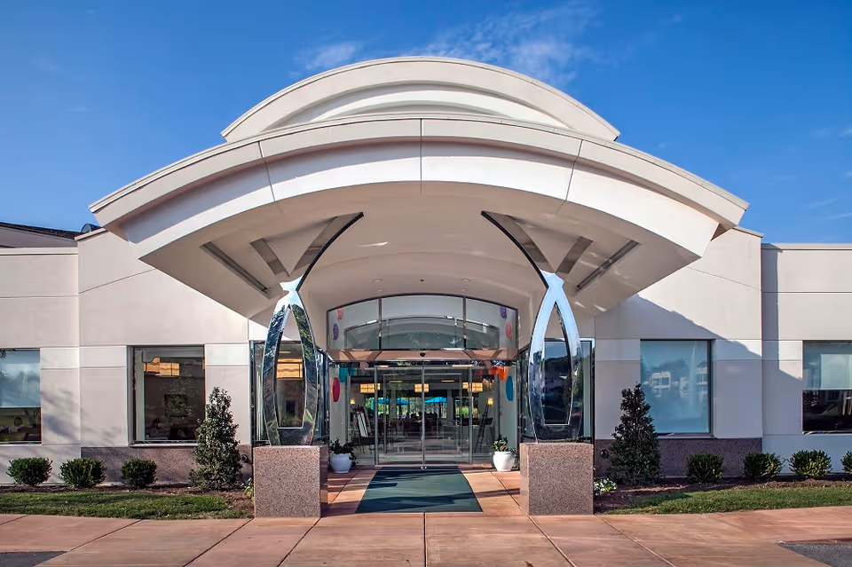 Modern senior living facility entrance with curved canopy and glass doors.