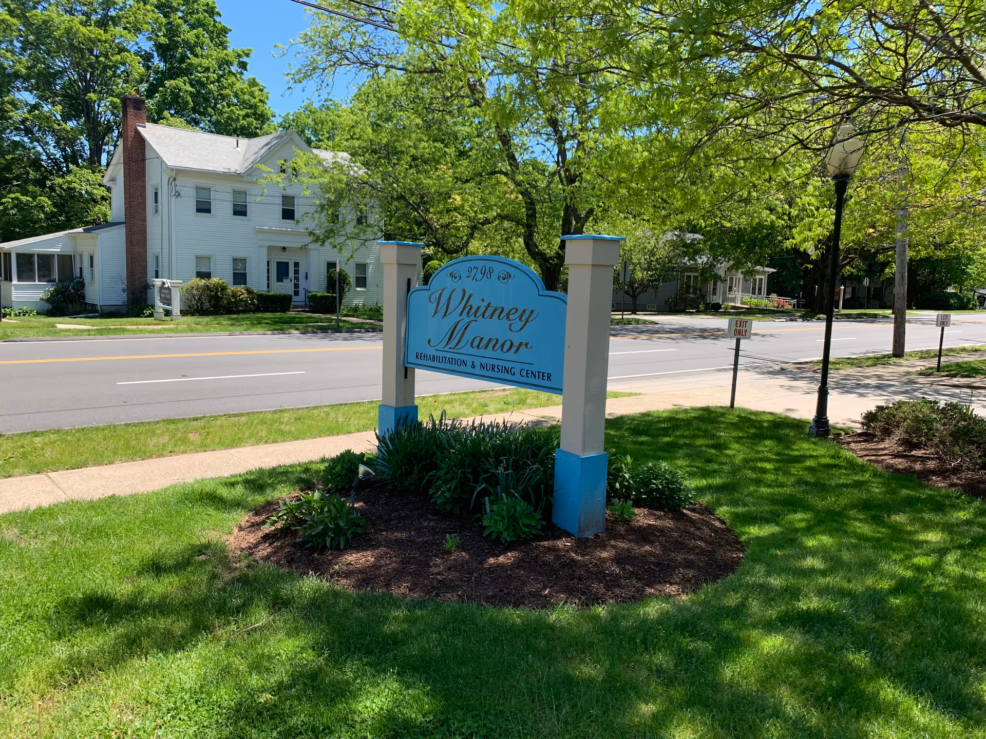 Exterior view of Whitney Manor Rehabilitation & Nursing Center with sign and green landscaping.