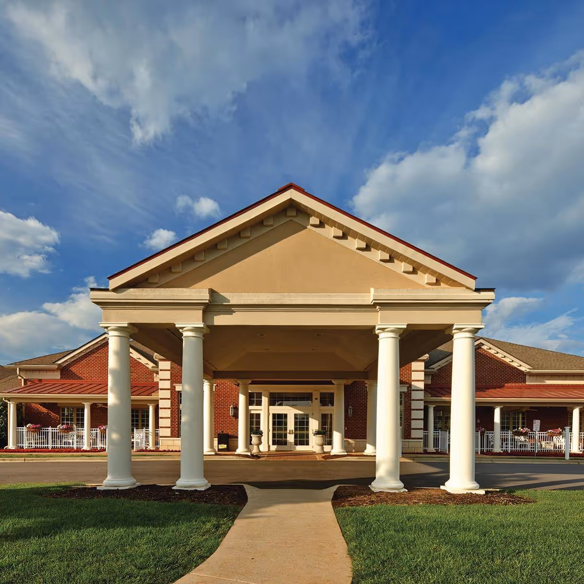 Sunny exterior view of Valhalla Post Acute's front entrance with columns and brick facade.