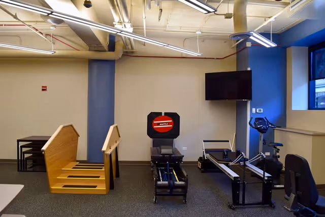 Therapy gym with stair equipment, treadmills, and a wall-mounted TV.