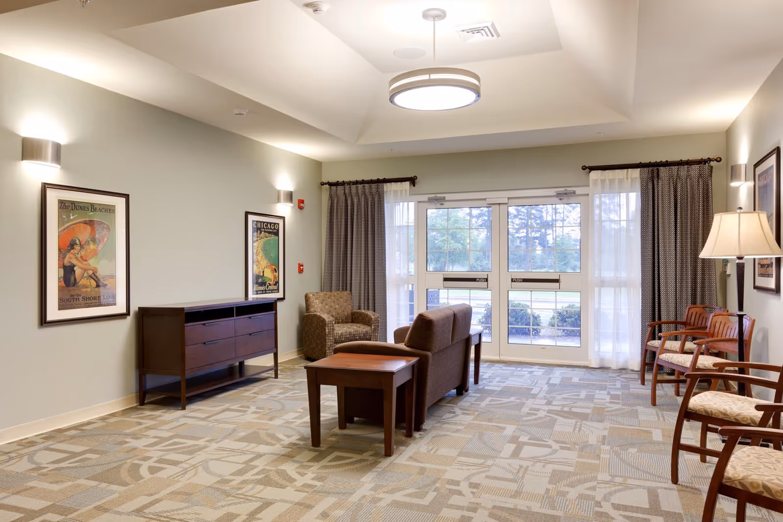 Cozy lounge area with seating, artwork, and glass doors in a senior living lobby.