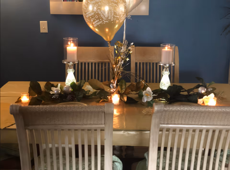 Decorated dining table with candles, greenery, and balloons in a blue dining room.