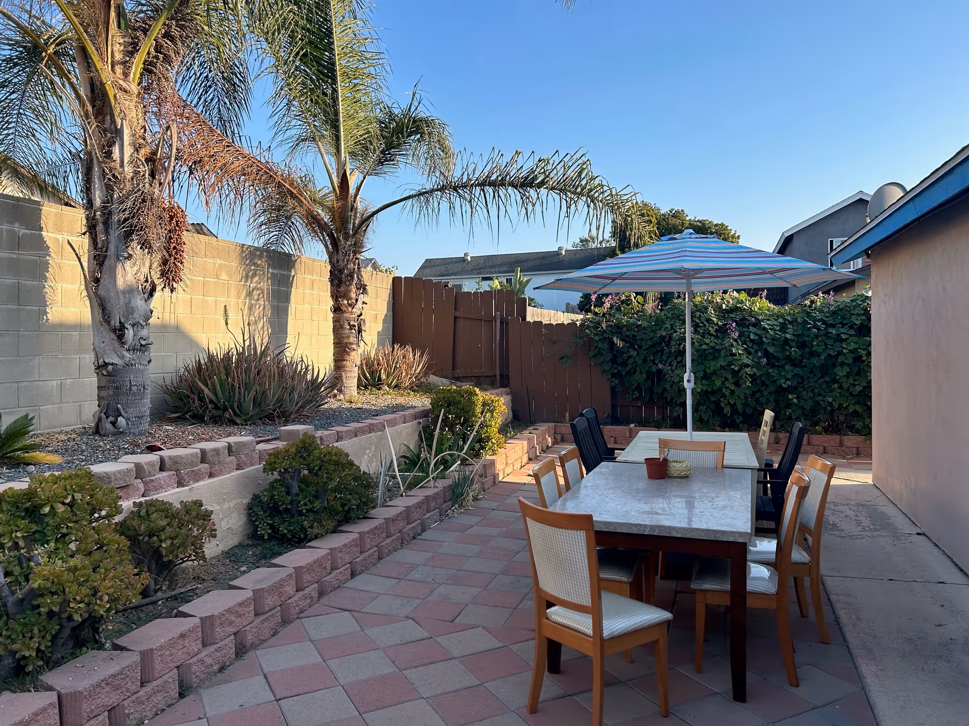 Outdoor courtyard at Elderly Haven with a dining table, chairs, umbrella, and tropical landscaping.