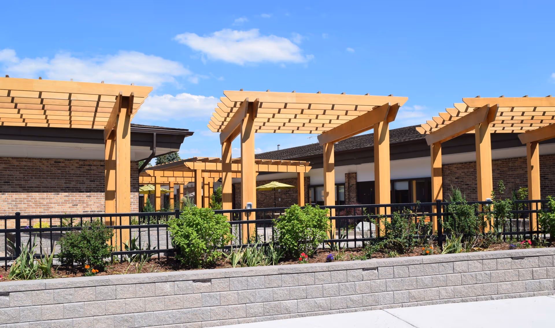 Exterior view of a brick senior facility with wooden pergolas and landscaped walkway.