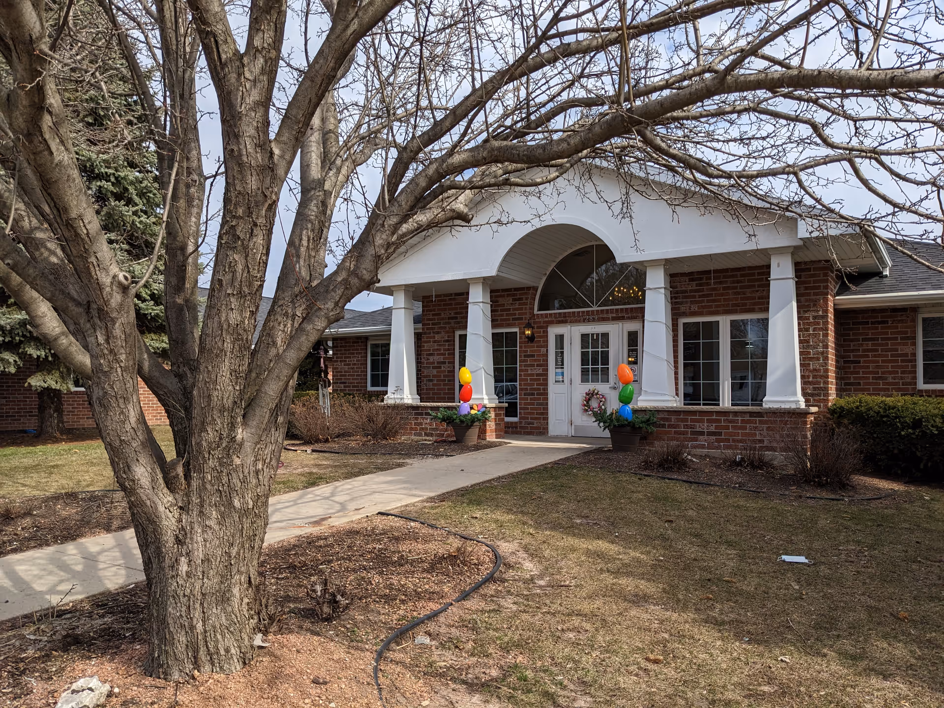 Front entrance of a brick senior living facility with balloons and wreaths.