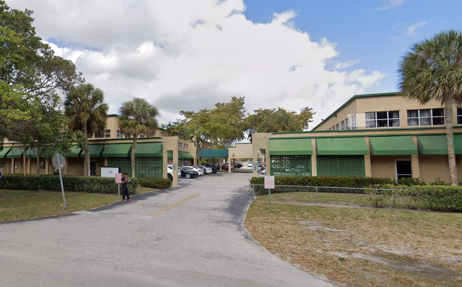 Exterior view of a beige senior care facility with green awnings and palm trees.