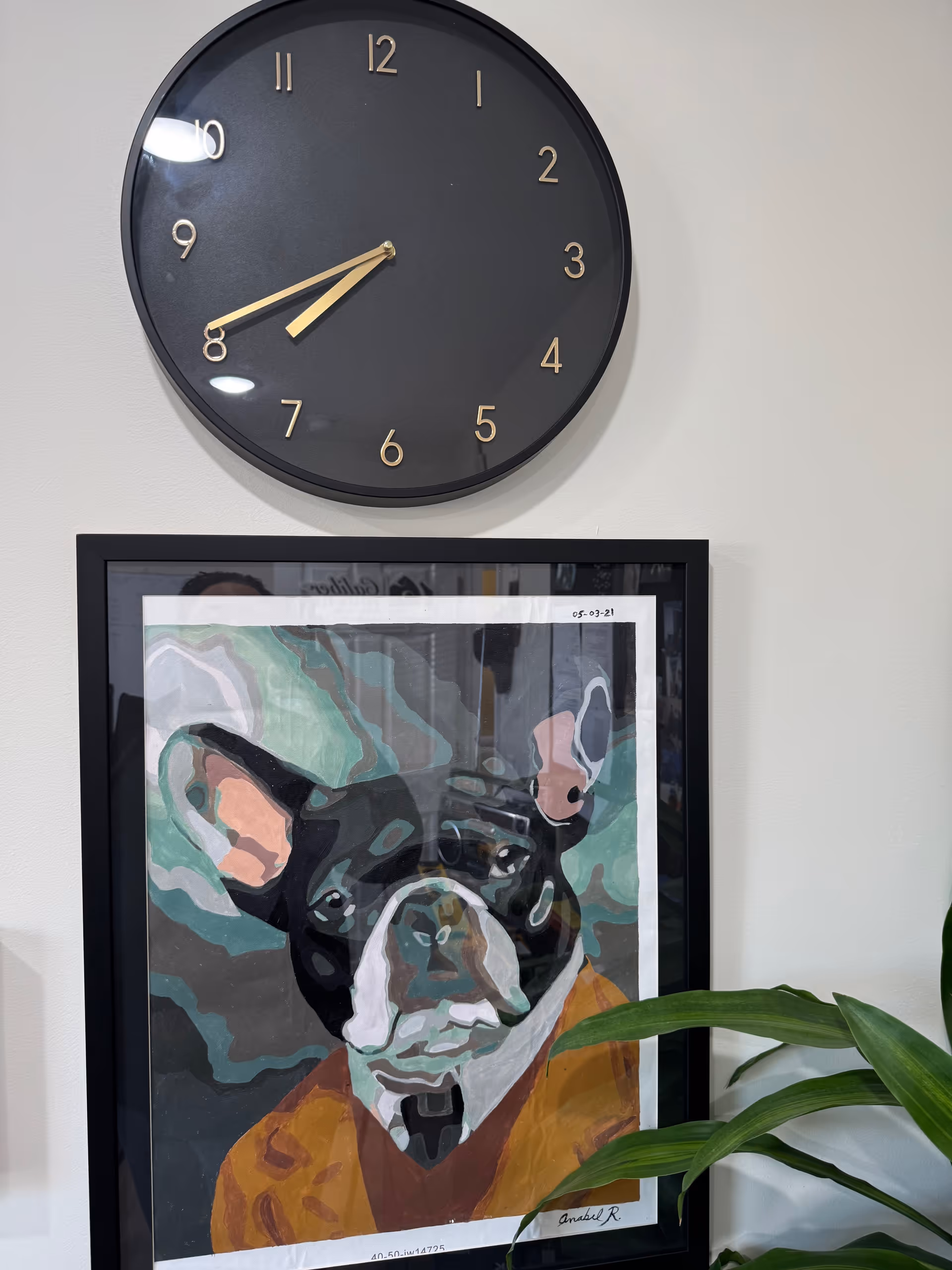 A large black clock and framed dog artwork hang on a light interior wall.