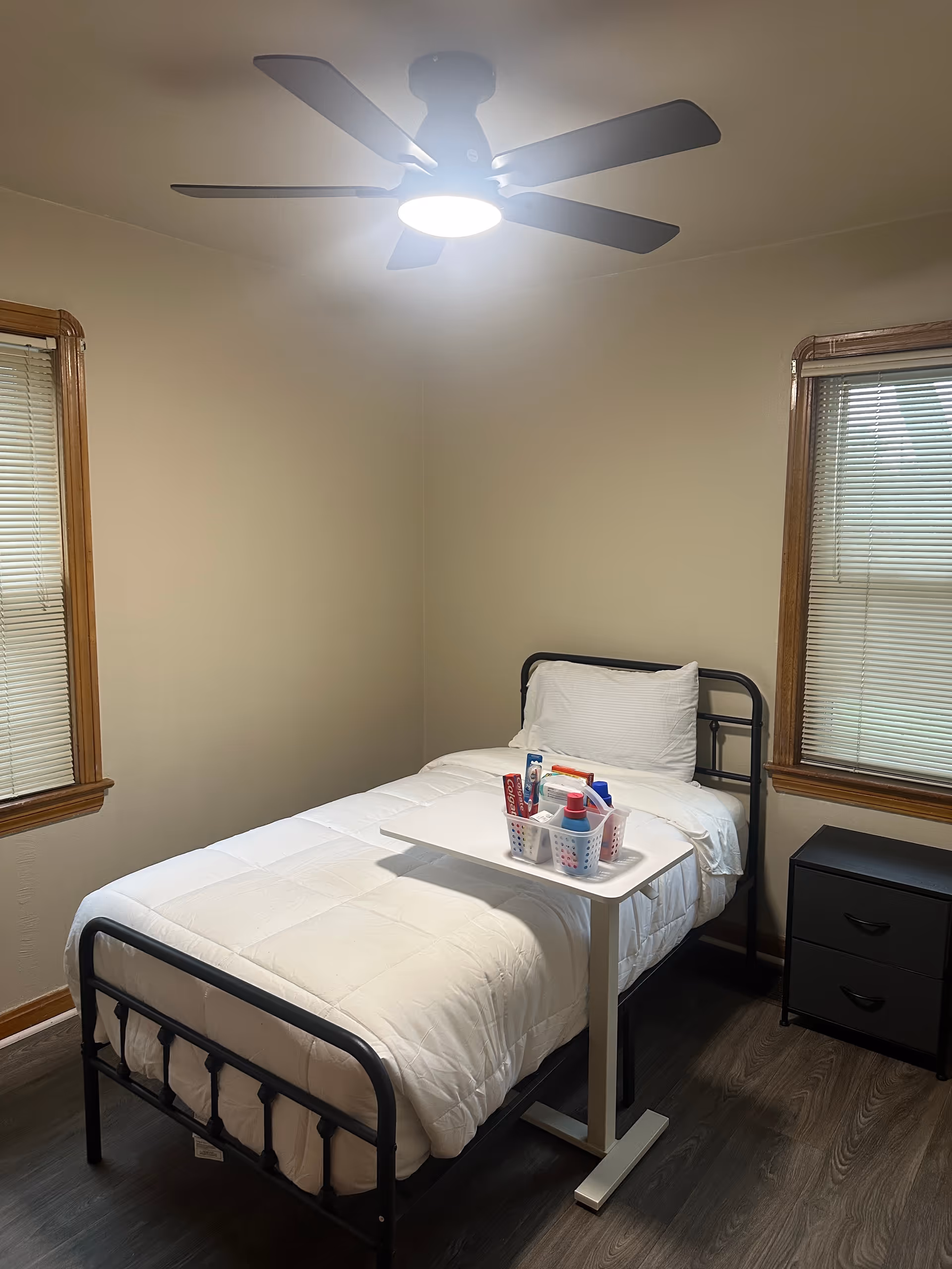 A small bedroom with a single bed, ceiling fan, and a nightstand in a resident room.