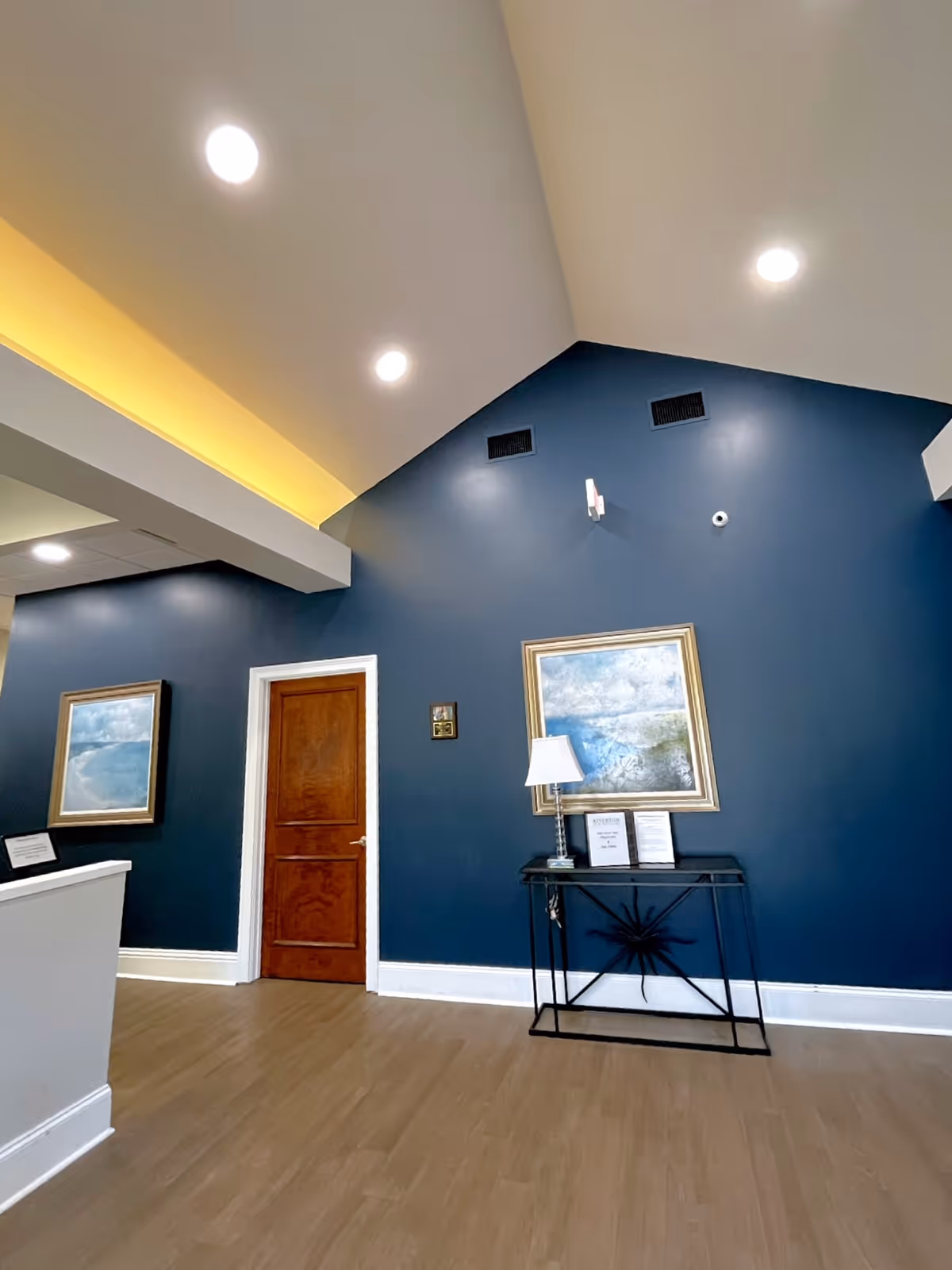 Interior reception area with dark blue walls, framed art, a wooden door, and a console table.