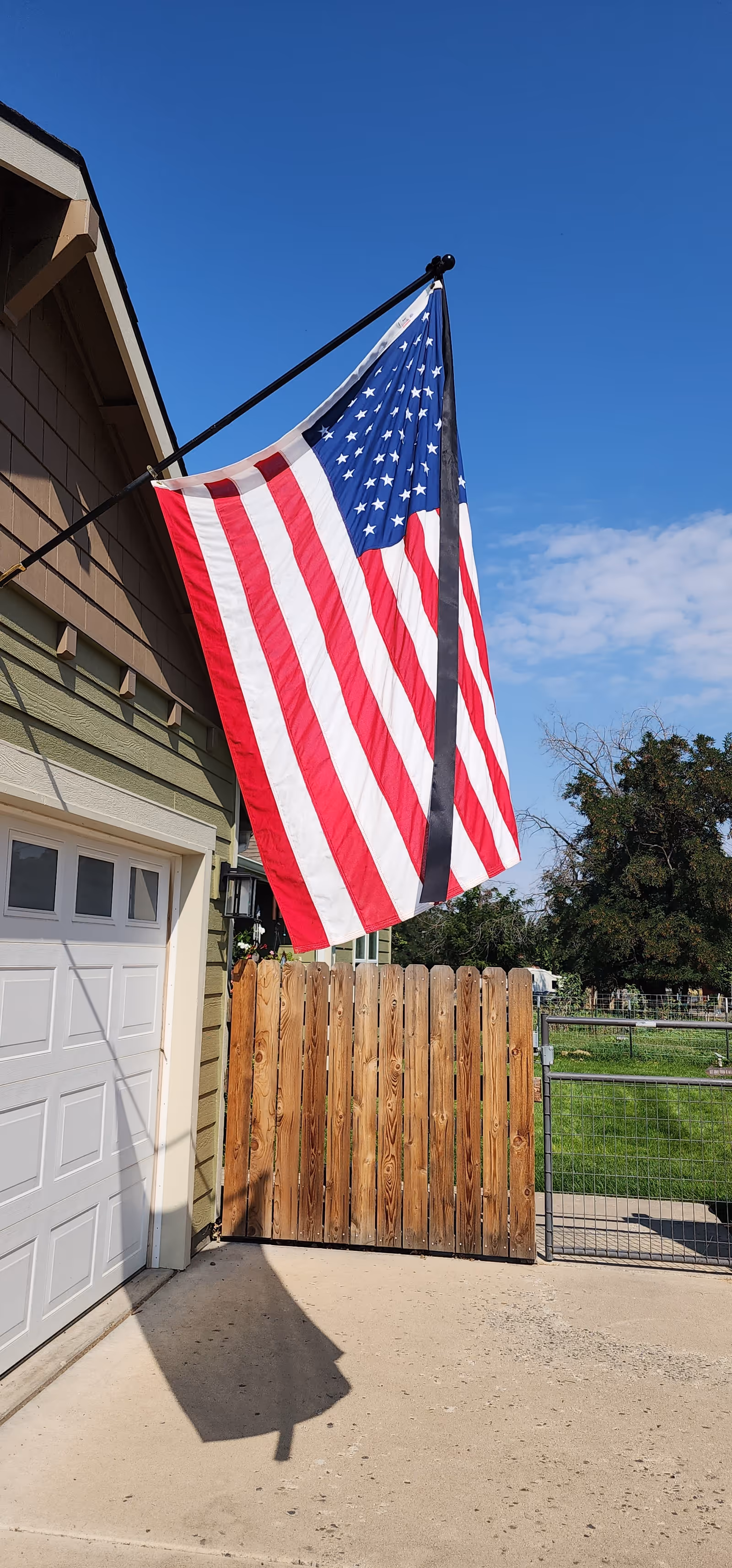 American flag on a house exterior beside a wooden gate and clear blue sky.