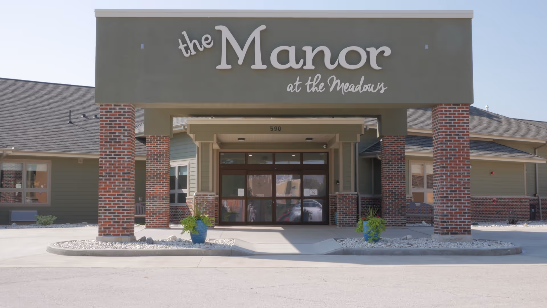 Front entrance of The Manor at the Meadows with brick columns and glass doors