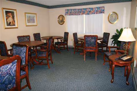 Carpeted senior living lounge/dining area with circular tables and upholstered chairs.